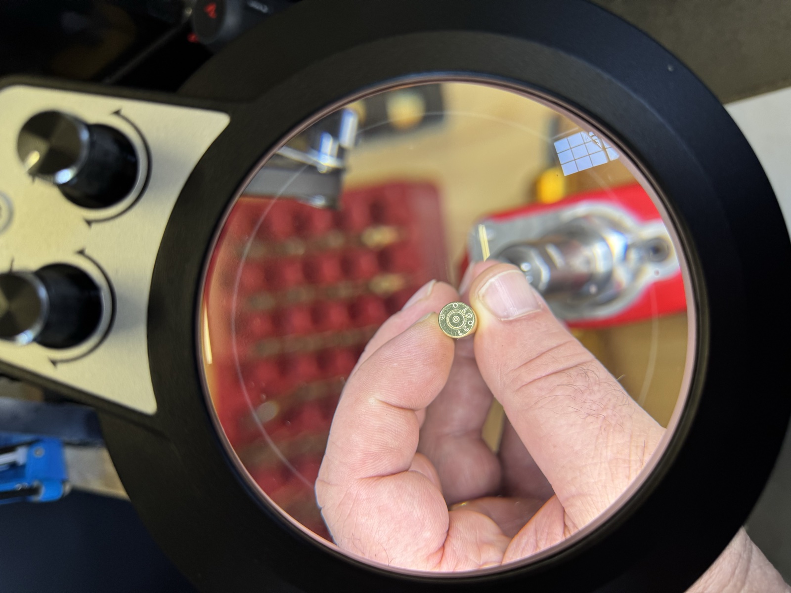 A case head held beneath the illuminated magnifier, sharply visible through the lens