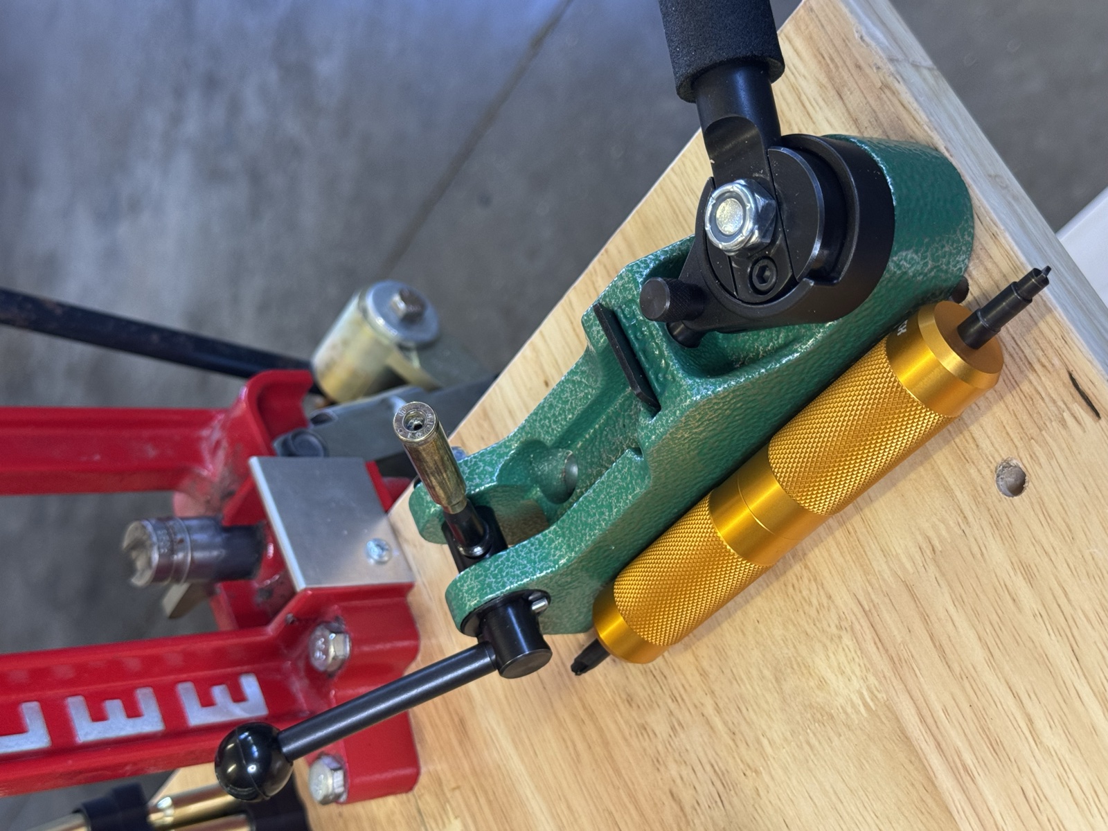 A green primer-pocket swager mounted at the edge of the reloading bench with the red Lee press behind it